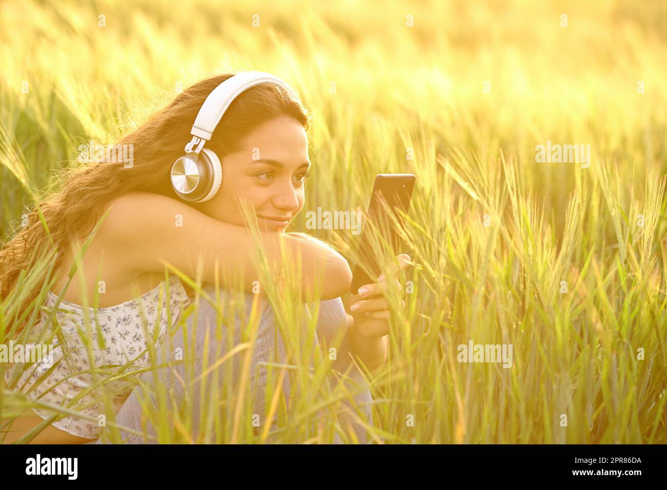 Femme au coucher du soleil dans un champ à l'écoute de la musique Banque D'Images