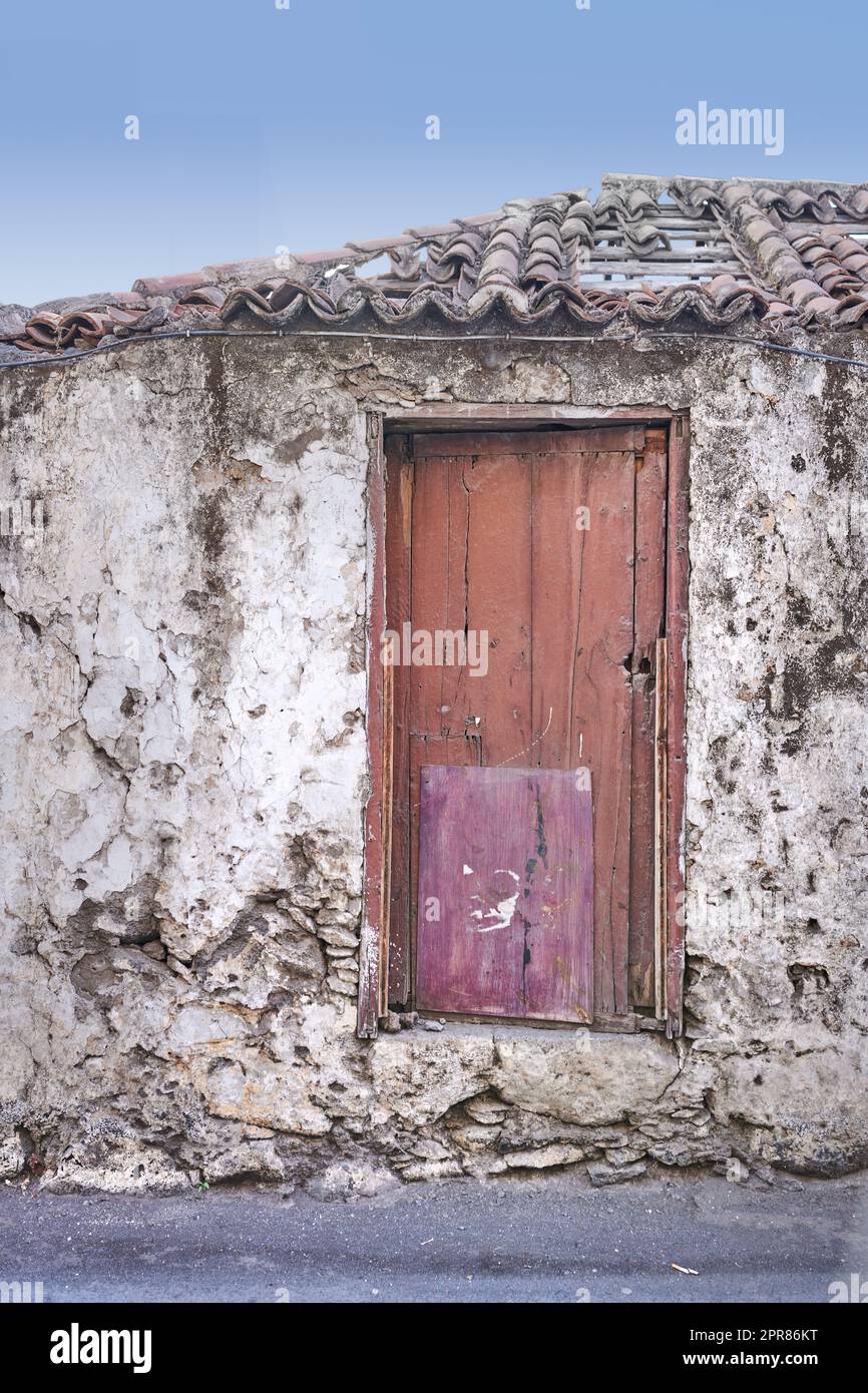 Ancienne maison abandonnée ou maison avec un mur en pierre et une porte en bois rouge. Bâtiment résidentiel ancien et ancien construit dans un style ou un design architectural traditionnel avec un fond bleu ciel Banque D'Images