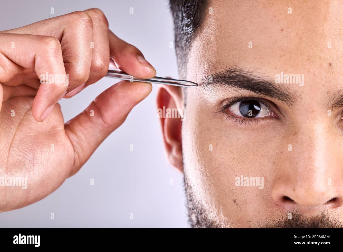 La qualité est presque parfaite. Gros plan d'un jeune homme en brossant ses sourcils sur un fond gris. Banque D'Images