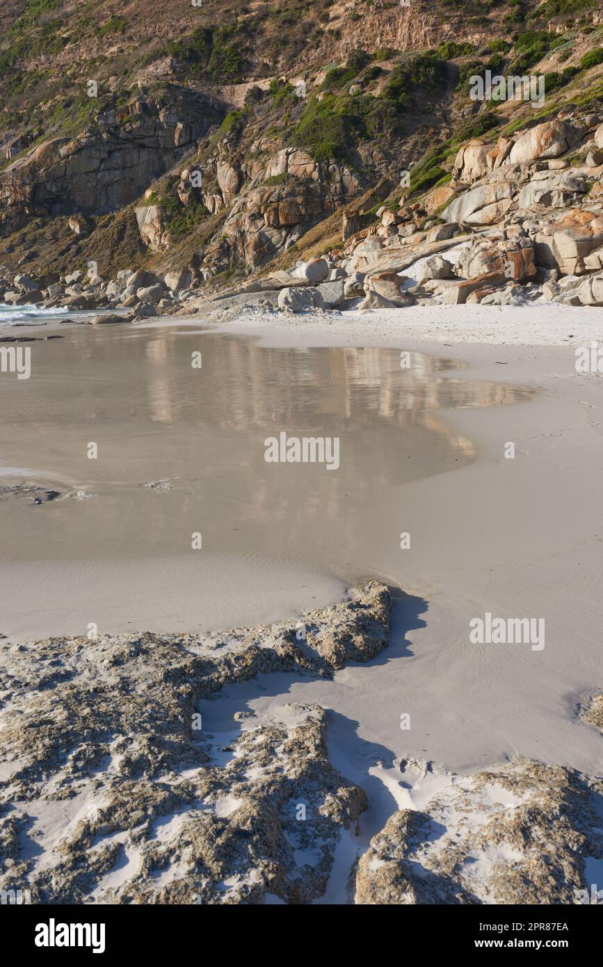 Une côte rocheuse à une plage du Cap avec des montagnes en arrière-plan et un espace d'imitation. Vue sur une rive avec des rochers à l'océan. La côte rocheuse de la mer de montagne se lavant au-dessus du sable de plage par temps froid Banque D'Images