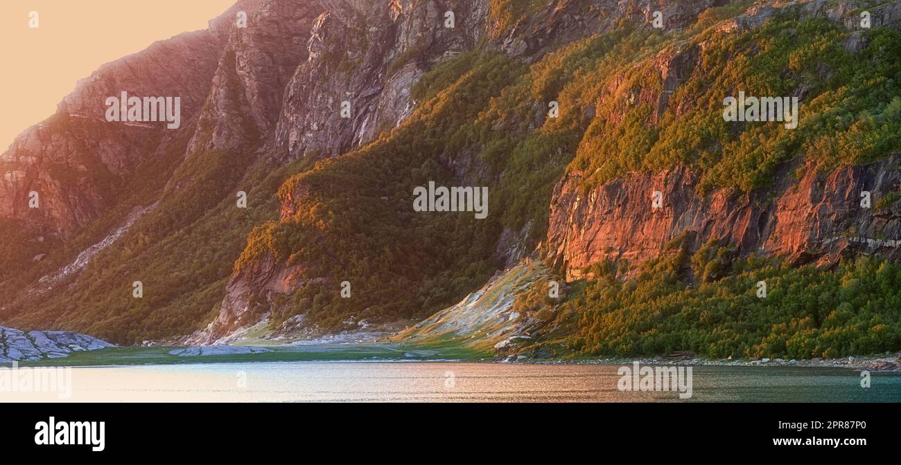 Vue sur le paysage de l'eau du lac et des montagnes au coucher du soleil en Norvège. Calme, serein, tranquille, océan ou mer à l'aube dans une campagne isolée et paisible. Paysage de fjord naturel reposant avec falaises abruptes à l'aube Banque D'Images