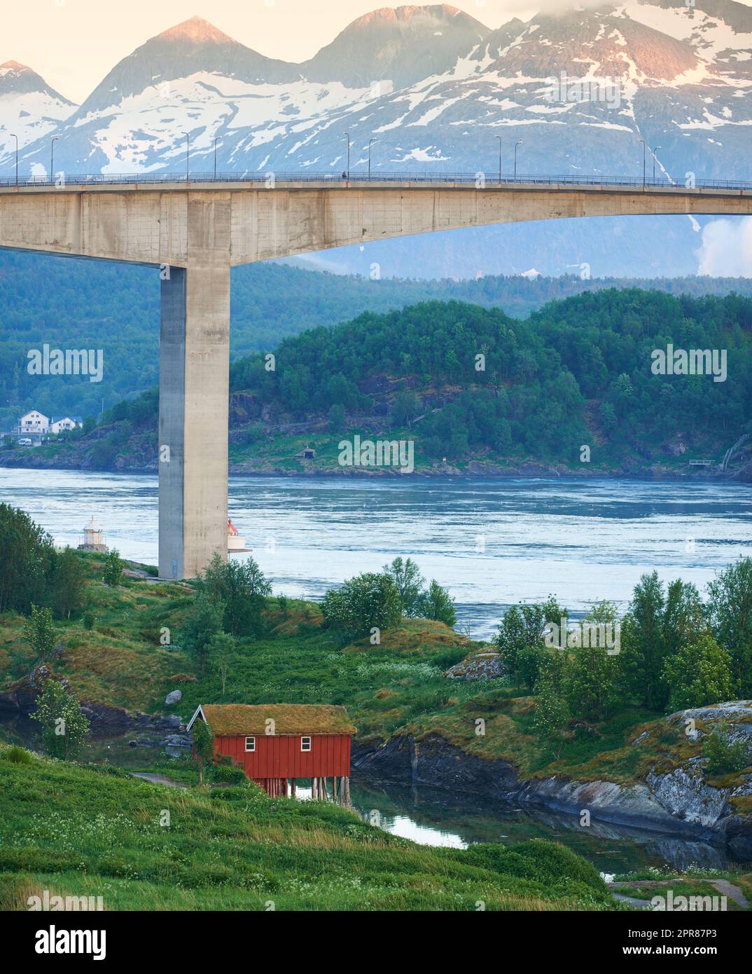 Vue sur le paysage du pont de Saltsaumen dans le Nordland, Norvège en hiver. Paysage d'infrastructure de transport au-dessus d'une rivière ou d'un ruisseau avec un fond de montagne enneigé. Une cabine isolée outre-mer Banque D'Images