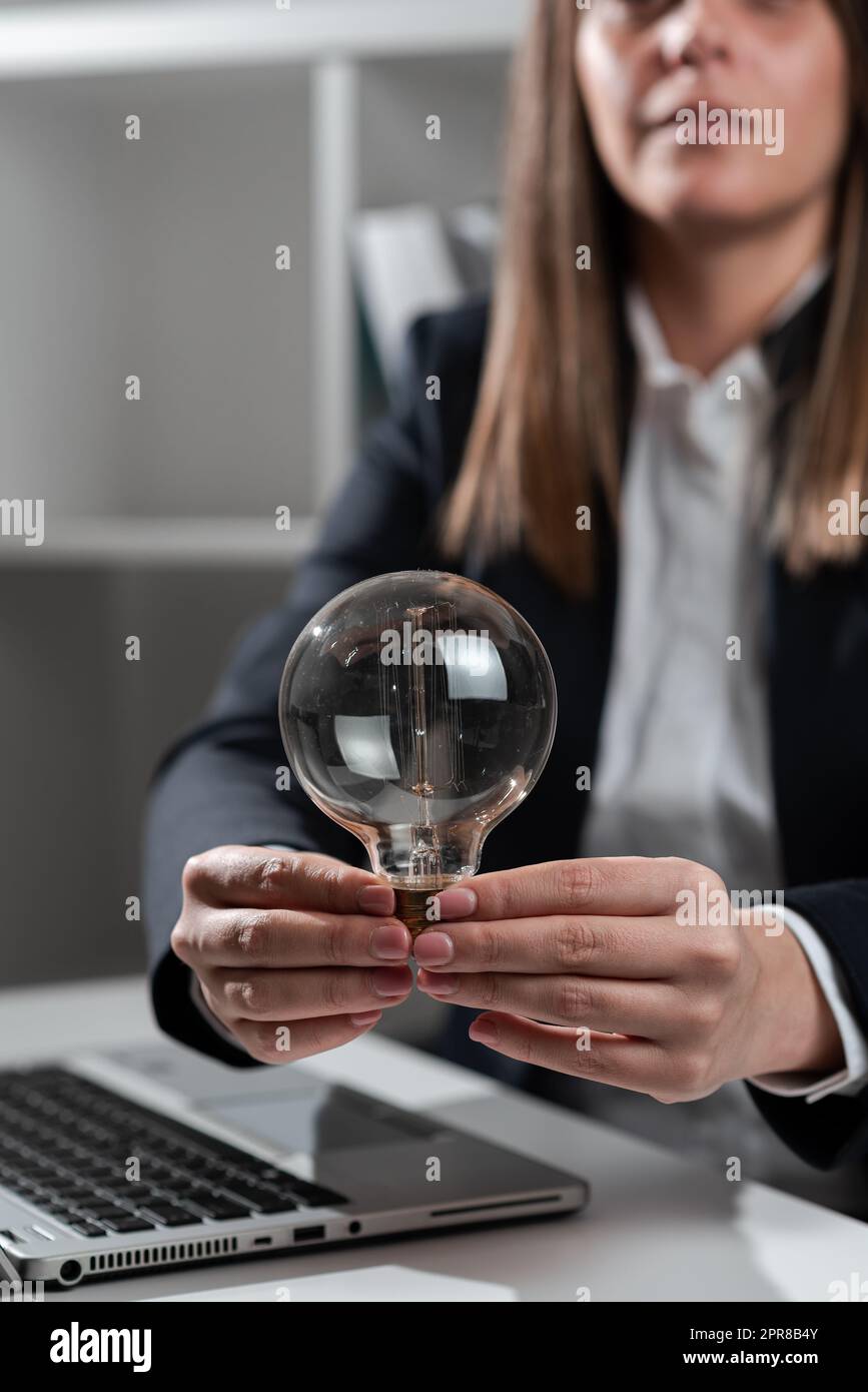 Femme d'affaires tenant une ampoule avec les deux mains au bureau. Femme en costume ayant de la lumière entre les paumes sur le bureau avec le dessus de tour et présentant des messages importants. Banque D'Images