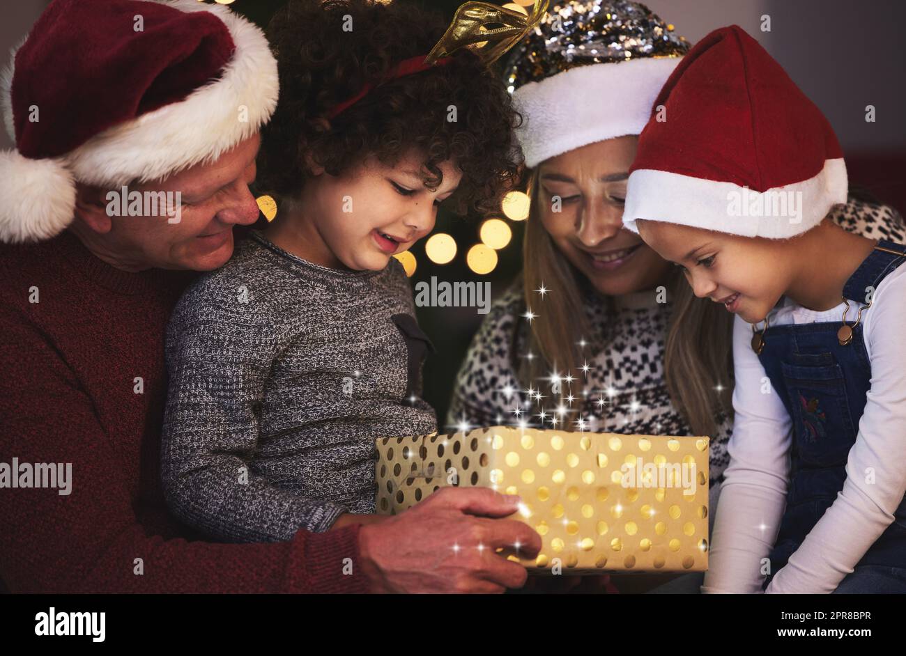 La famille est le plus grand cadeau de tous. Une famille ouvrant un cadeau de Chrstmas ensemble à la maison. Banque D'Images