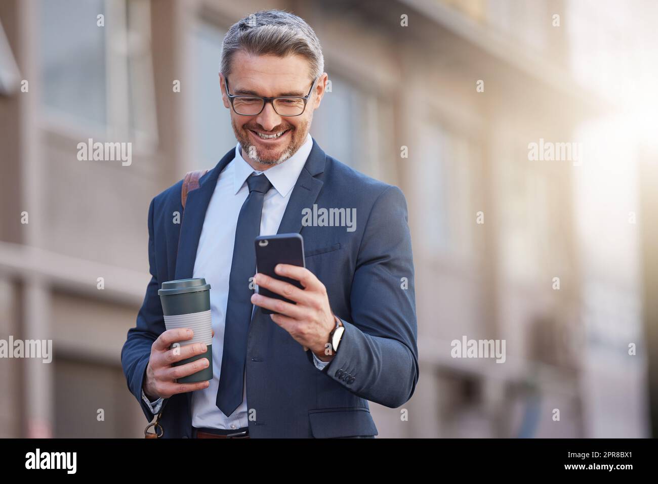 Il vient d'avoir de bonnes nouvelles : un homme d'affaires mature qui boit un café tout en utilisant un téléphone dans la ville. Banque D'Images