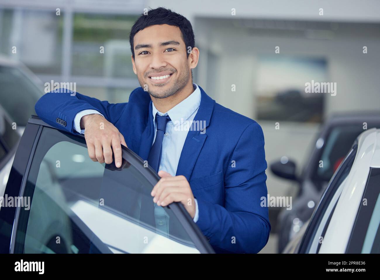 Je trouve la voiture parfaite pour vous. Portrait court d'un jeune vendeur de voitures de sexe masculin qui travaille sur le sol de la salle d'exposition. Banque D'Images