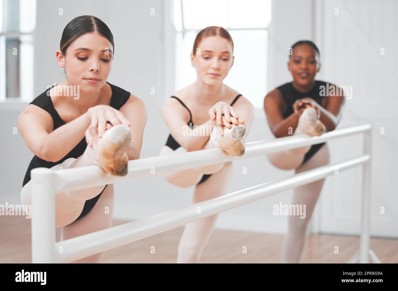 Les danseuses de ballet ont un talent pour faire paraître le ballet sans effort. Photo d'un groupe de danseurs de ballet se penchant contre une barre. Banque D'Images