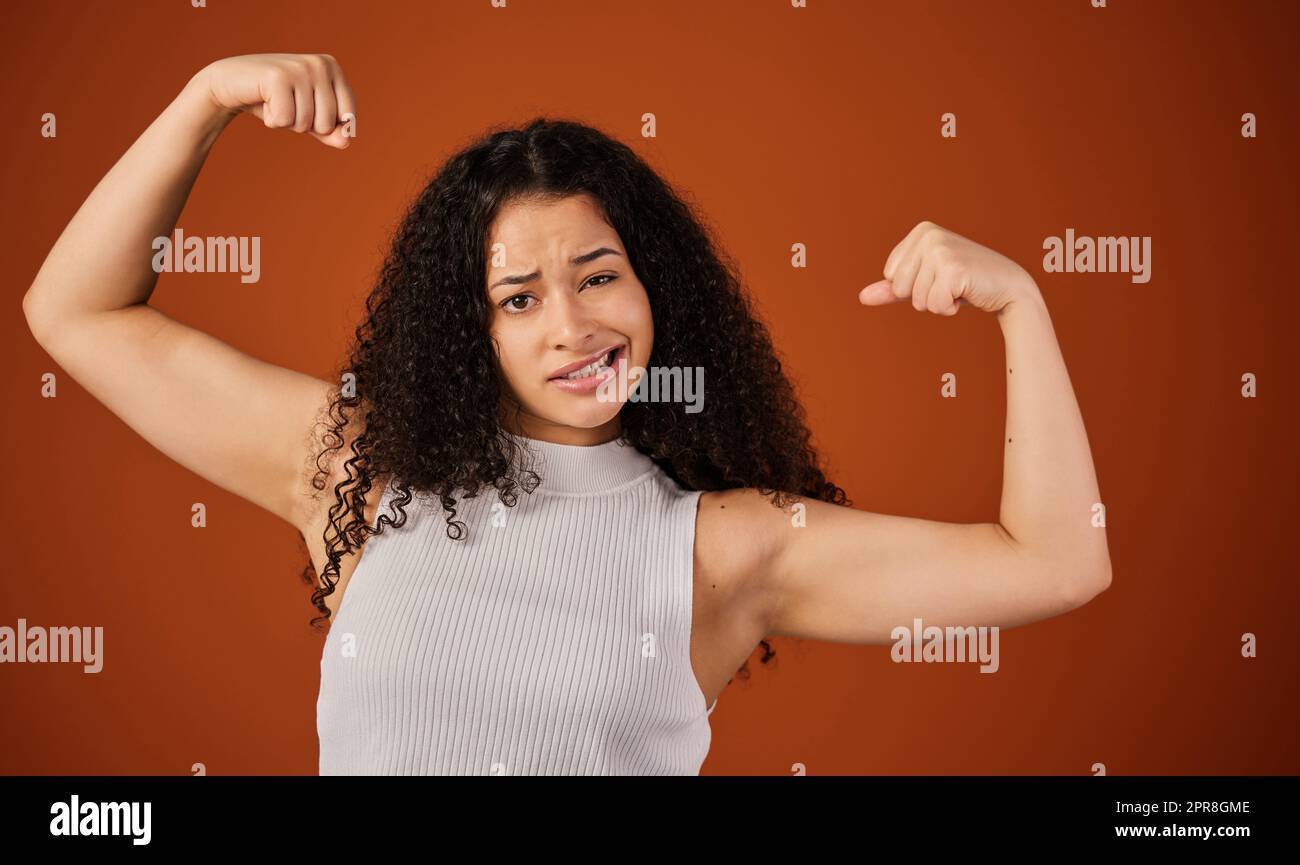 Je suis fou fort. Portrait rogné d'une jeune femme attrayante en flexion de son biceps en studio sur un fond rouge. Banque D'Images