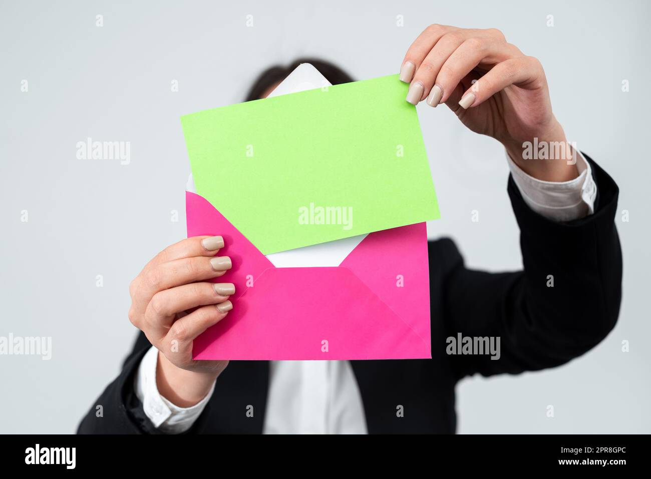 Mains de la femme d'affaires mettant une lettre importante dans l'enveloppe pour l'envoi par courrier. Femme portant un costume tenant une carte postale avec des informations d'affaires et un message essentiels. Banque D'Images