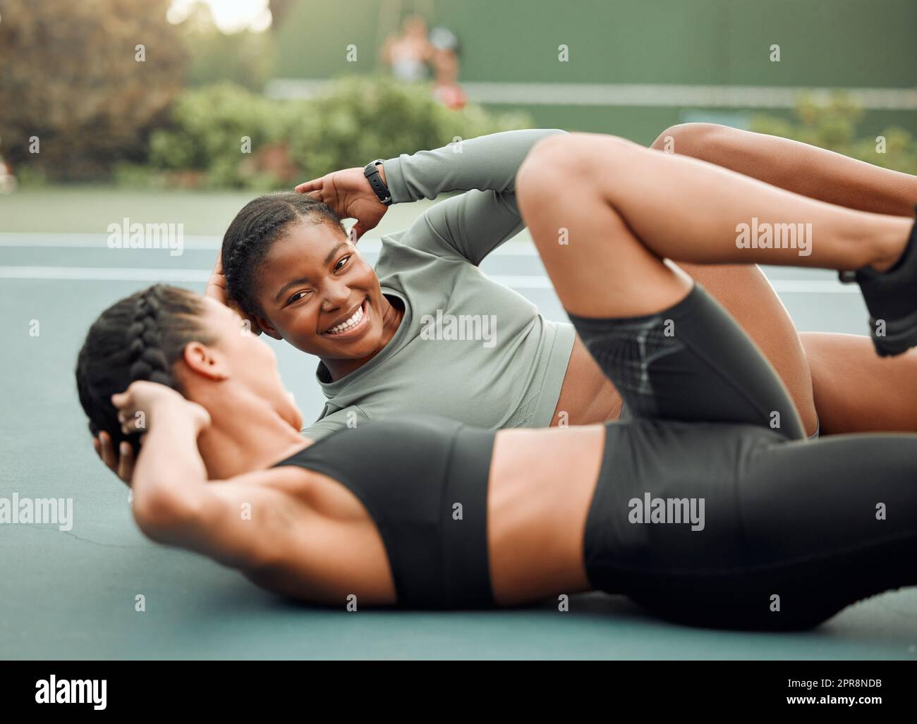 La motivation est à vos côtés. Deux jeunes athlètes féminines attirantes qui élèvent les jambes pendant leur entraînement sur un terrain de sport. Banque D'Images
