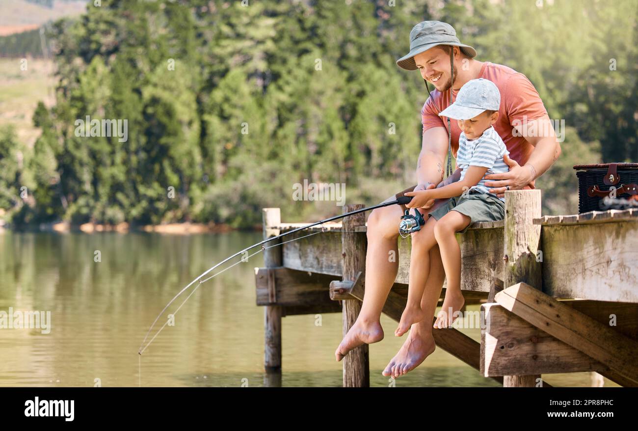 Eh bien, un petit garçon pêchant avec son père sur un lac dans une forêt, vous vous émerveillez bientôt devant un petit poisson. Banque D'Images