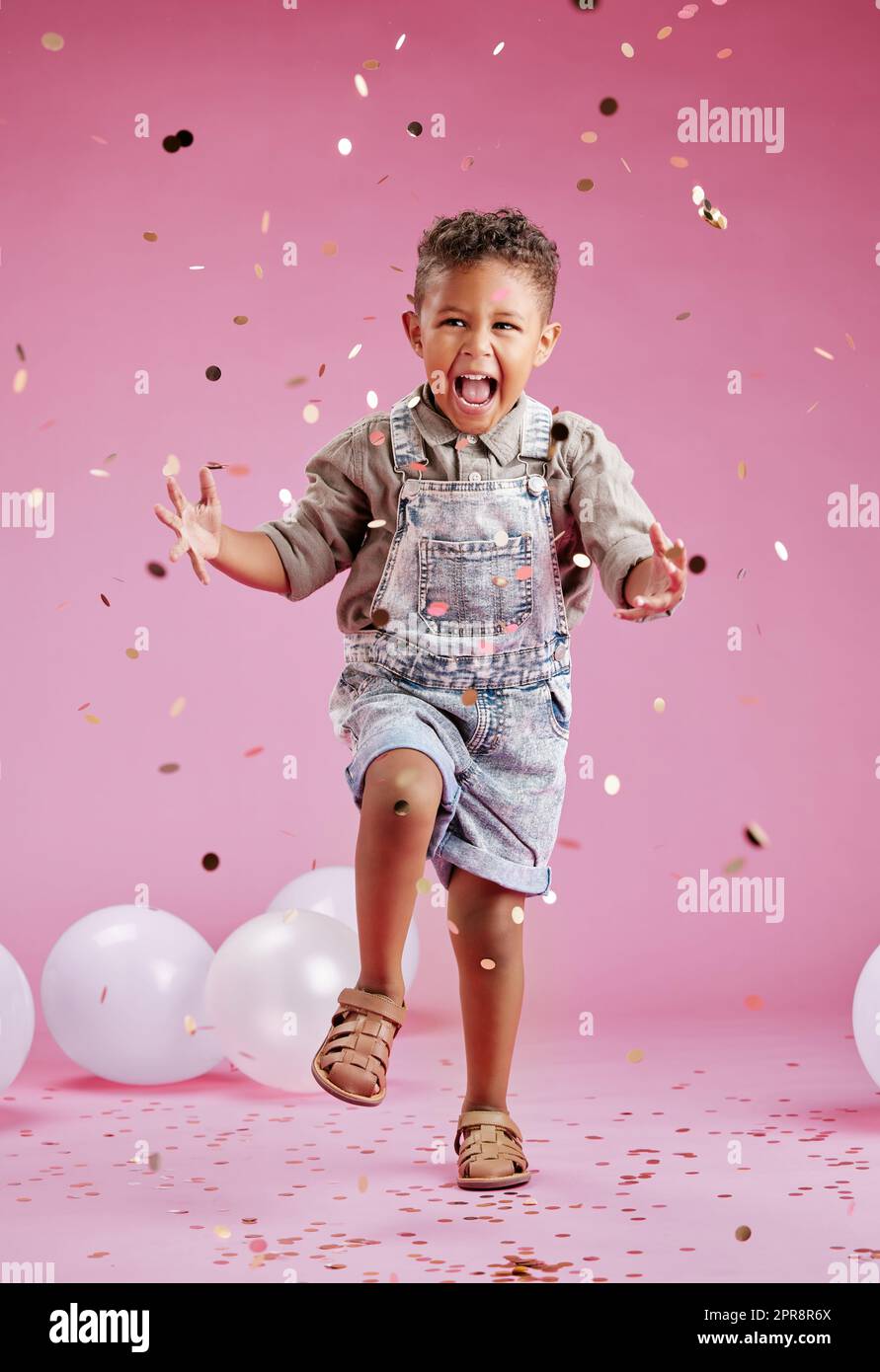 Un mignon petit garçon de course mixte célébrant et gagnant contre un arrière-plan rose copyspace dans un studio. Enfant africain regardant excité à une fête de révélation de genre avec des confetti et des ballons Banque D'Images