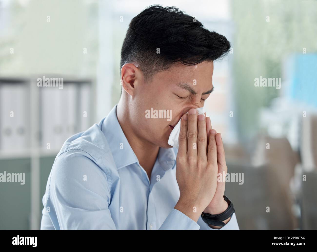 Un homme d'affaires asiatique malade soufflant le nez avec des tissus tout en travaillant dans un bureau. Guy se sent mal avec la grippe, le rhume et les symptômes de covid. Souffrant de congestion, de sinus et d'allergies saisonnières au printemps Banque D'Images