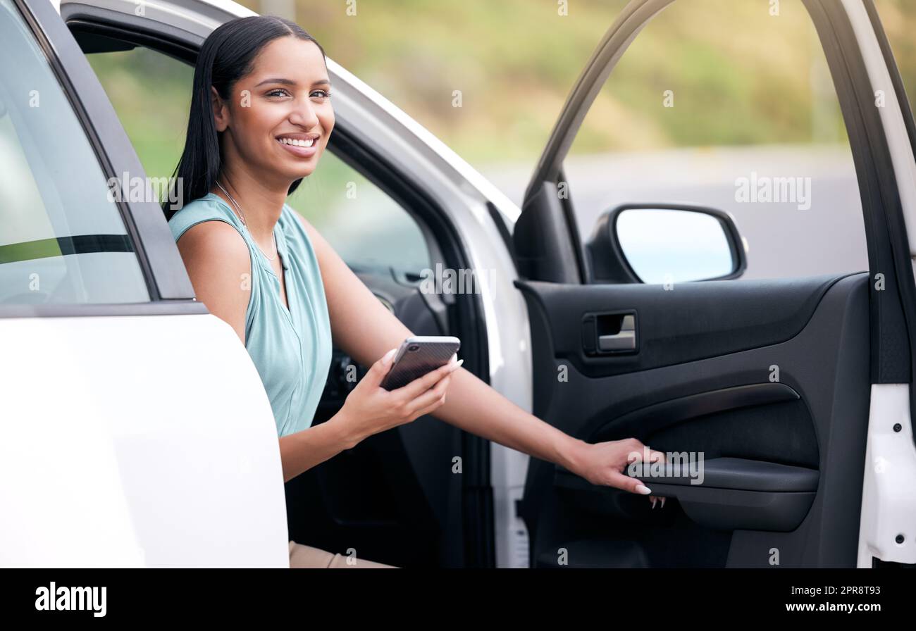 Une jeune femme d'affaires de race mixte tapant un message sur un téléphone tout en étant assise dans une voiture. Heureuse femme hispanique utilisant les médias sociaux tout en tenant son téléphone et assis dans une voiture seule Banque D'Images