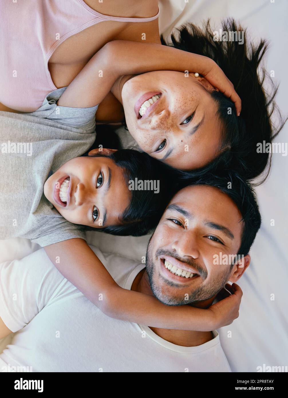 Bonne famille sur le lit. Portrait de famille heureuse d'en haut. Famille multiraciale au lit. Bonne fille se détendant avec ses parents. Les jeunes parents se liant à leur fille Banque D'Images