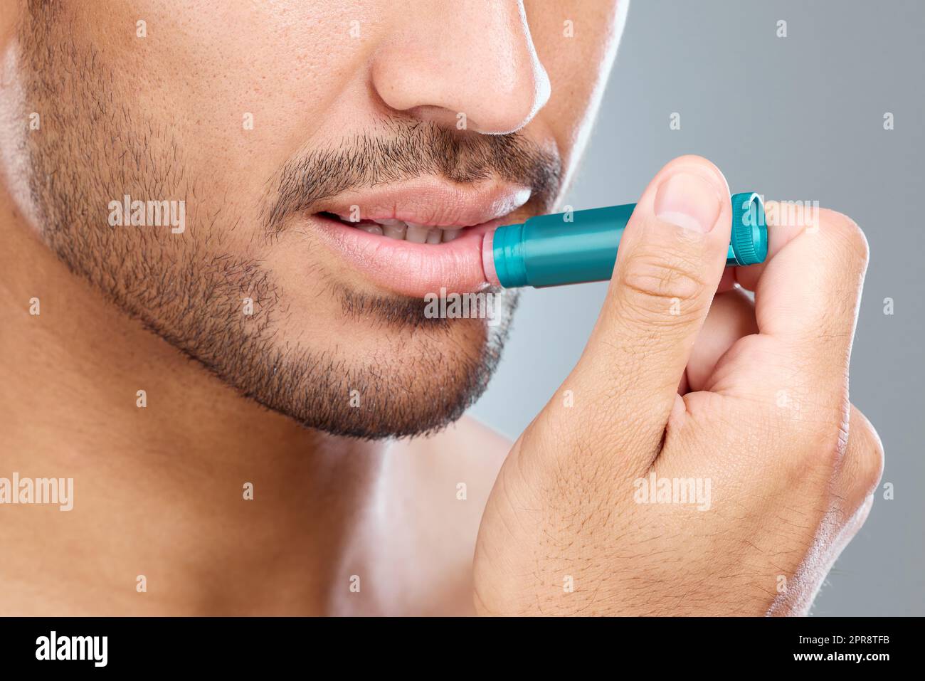 Vanquish les lèvres sèches. Un homme appliquant le baume des lèvres tout en  se tenant sur un fond gris Photo Stock - Alamy