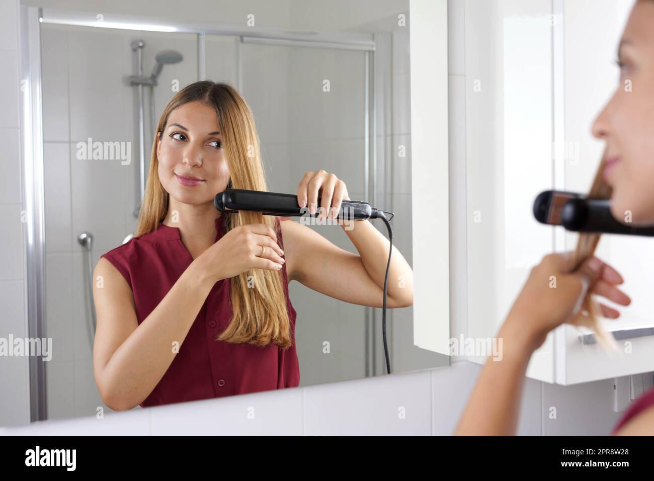Gros plan de la jeune femme latin utilisant un lisseur vapeur pour coiffer les cheveux dans le miroir de la salle de bains Banque D'Images