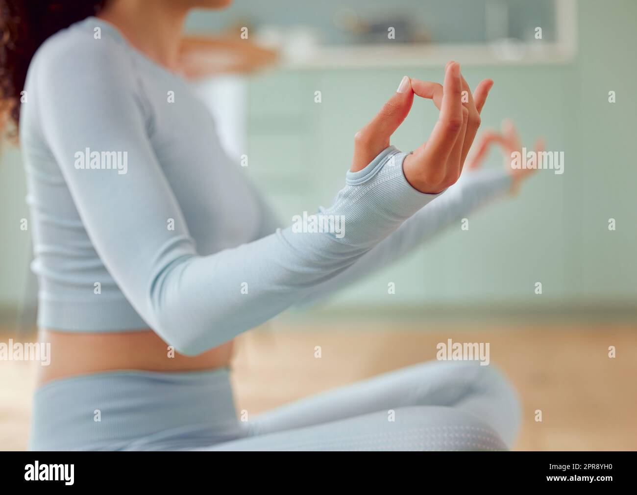 Gros plan jeune femme de course mixte méditant dans la position d'asana tout en pratiquant le yoga à la maison. Femme méconnaissable exerçant son corps et son esprit, trouvant la paix intérieure, l'équilibre et la clarté Banque D'Images