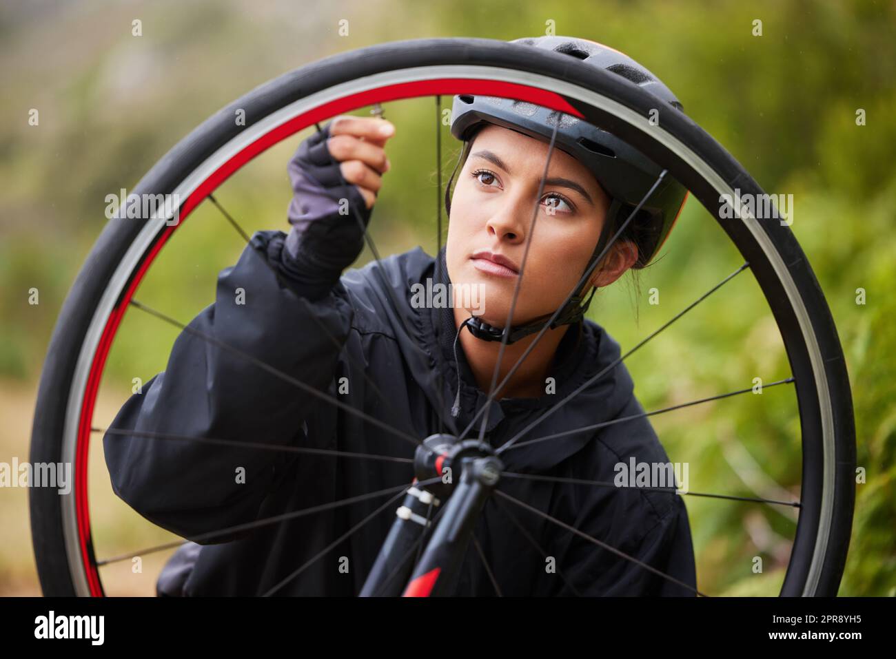 Une jeune femme athlétique qui fixe la roue d'un vélo tout en faisant du vélo à l'extérieur. Une femme sportive porte un casque et vérifie la pression d'air d'un pneu de vélo pour les réparations tout en conduisant dehors pour l'exercice Banque D'Images