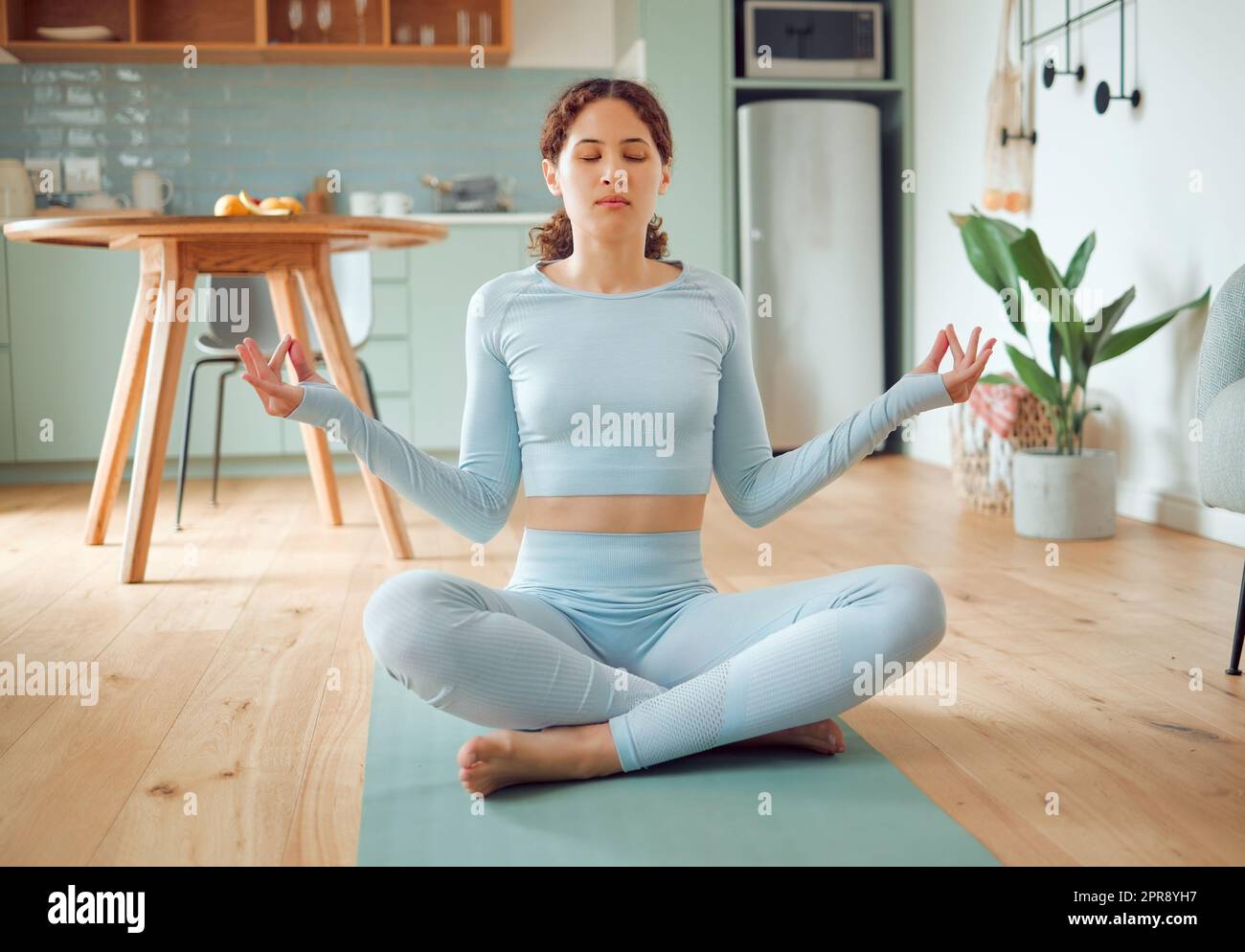 Belle jeune femme de course mixte méditant dans la position d'asana tout en pratiquant le yoga à la maison. Femme hispanique exerçant son corps et son esprit, trouvant la paix intérieure, l'équilibre et la clarté Banque D'Images