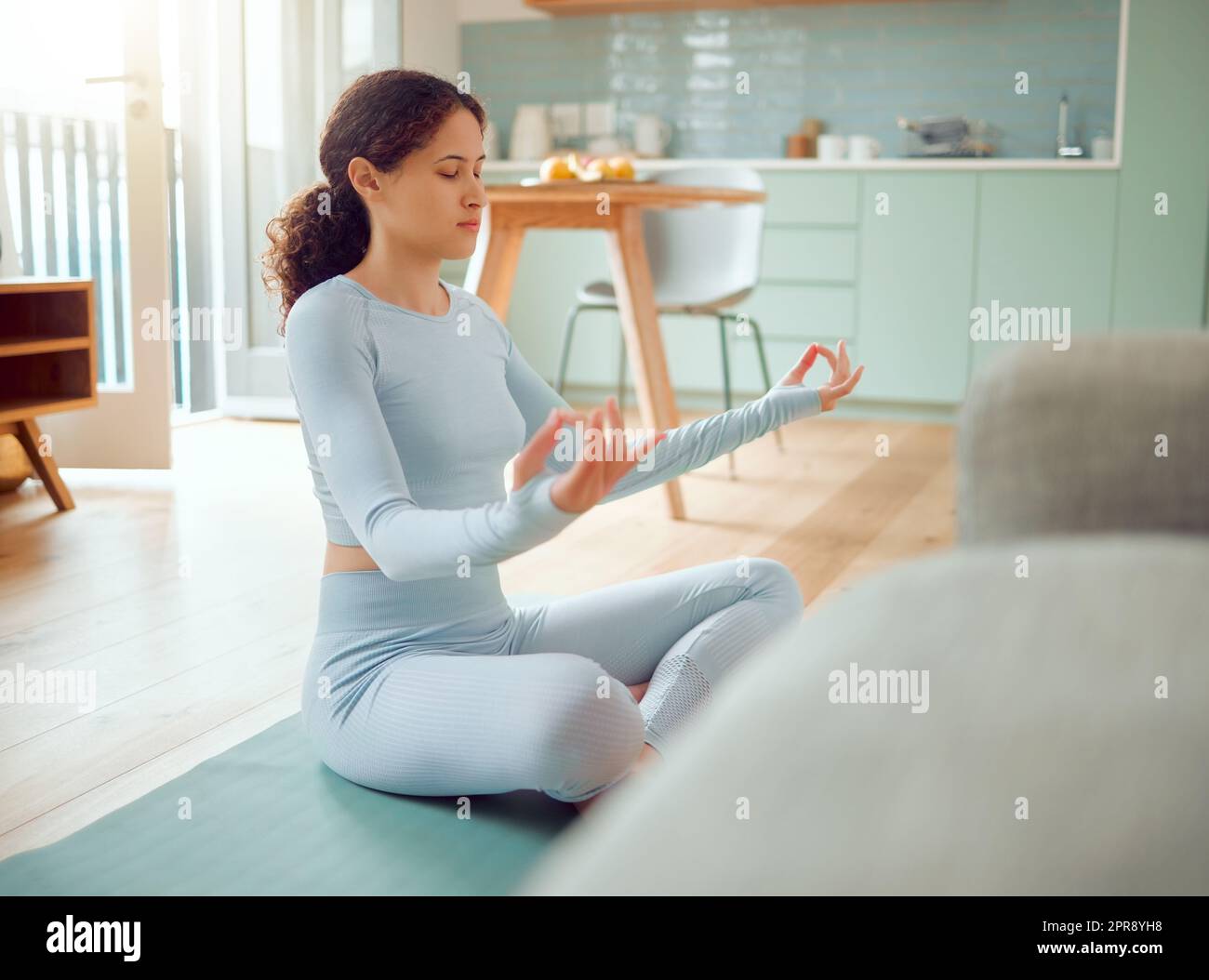 Belle jeune femme de course mixte méditant dans la position d'asana tout en pratiquant le yoga à la maison. Femme hispanique exerçant son corps et son esprit, trouvant la paix intérieure, l'équilibre et la clarté Banque D'Images