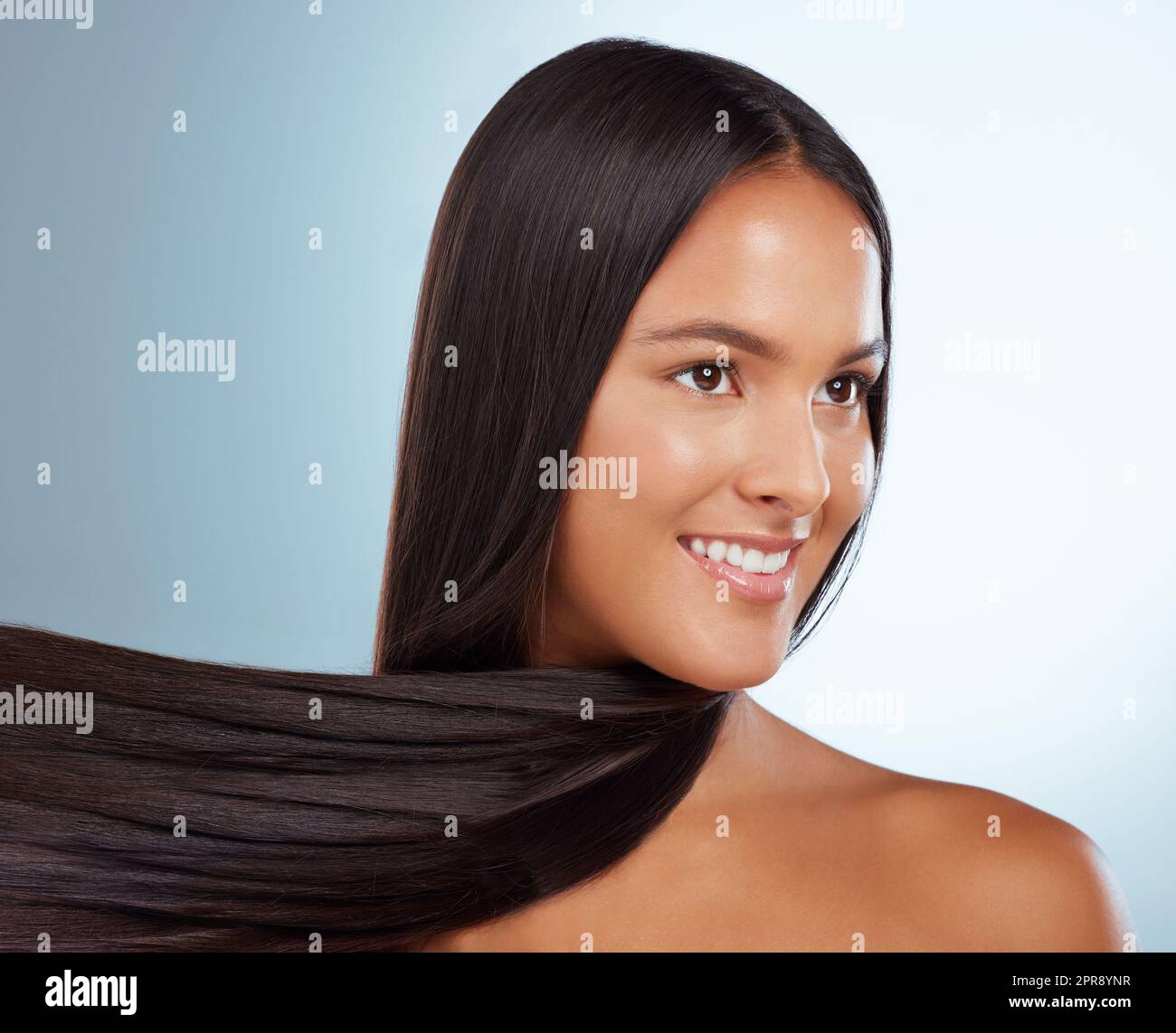 Une femme hispanique brune avec de longs cheveux luxuriants beau posant et souriant sur un fond gris studio. Race mixte femelle debout montrant ses beaux cheveux sains Banque D'Images