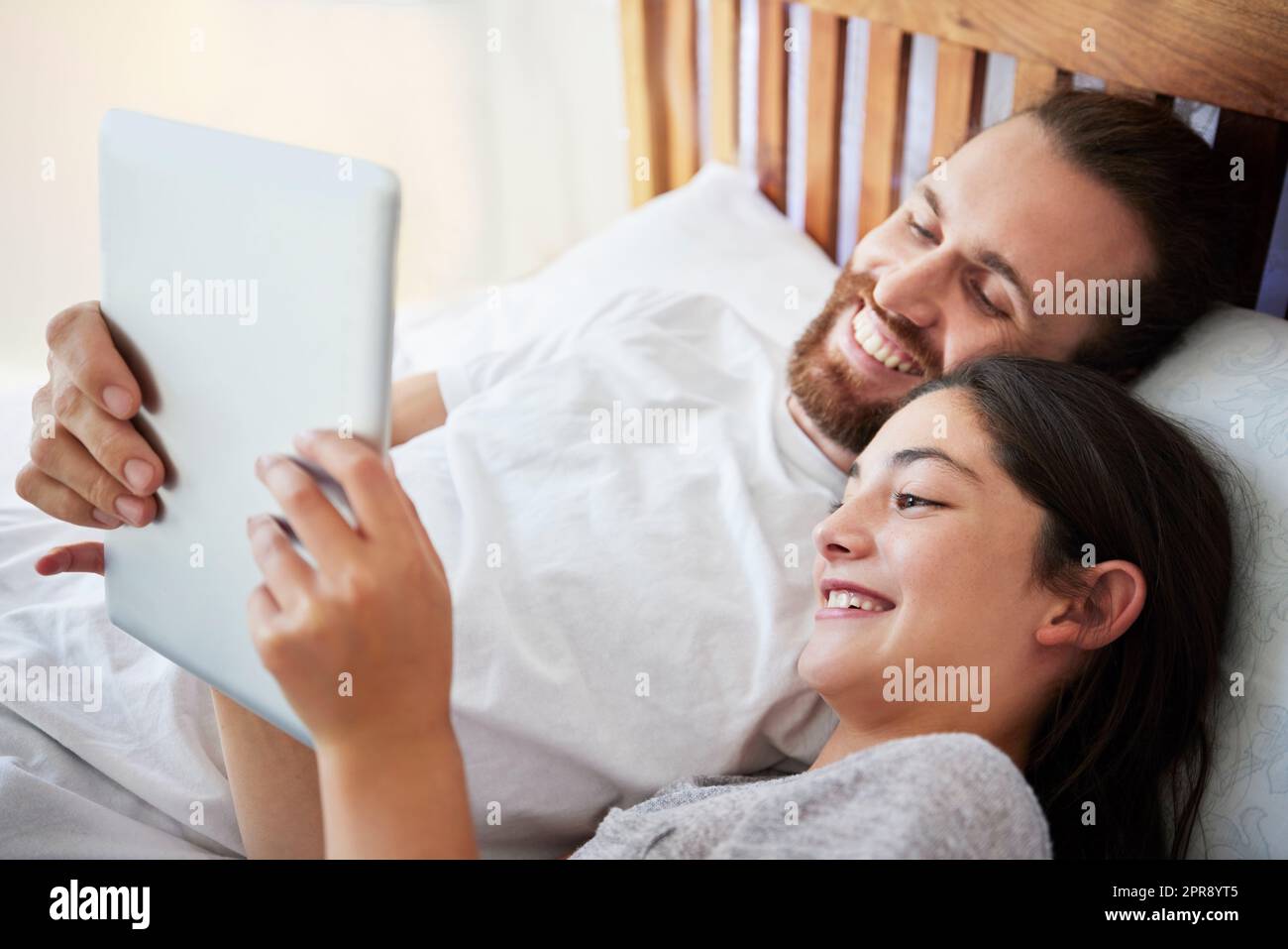 Joyeux père et fille caucasien tenant une tablette numérique tout en étant allongé ensemble sur un lit. Adolescente et papa regardant un film en ligne ou jouant au jeu tout en passant du temps à la maison Banque D'Images