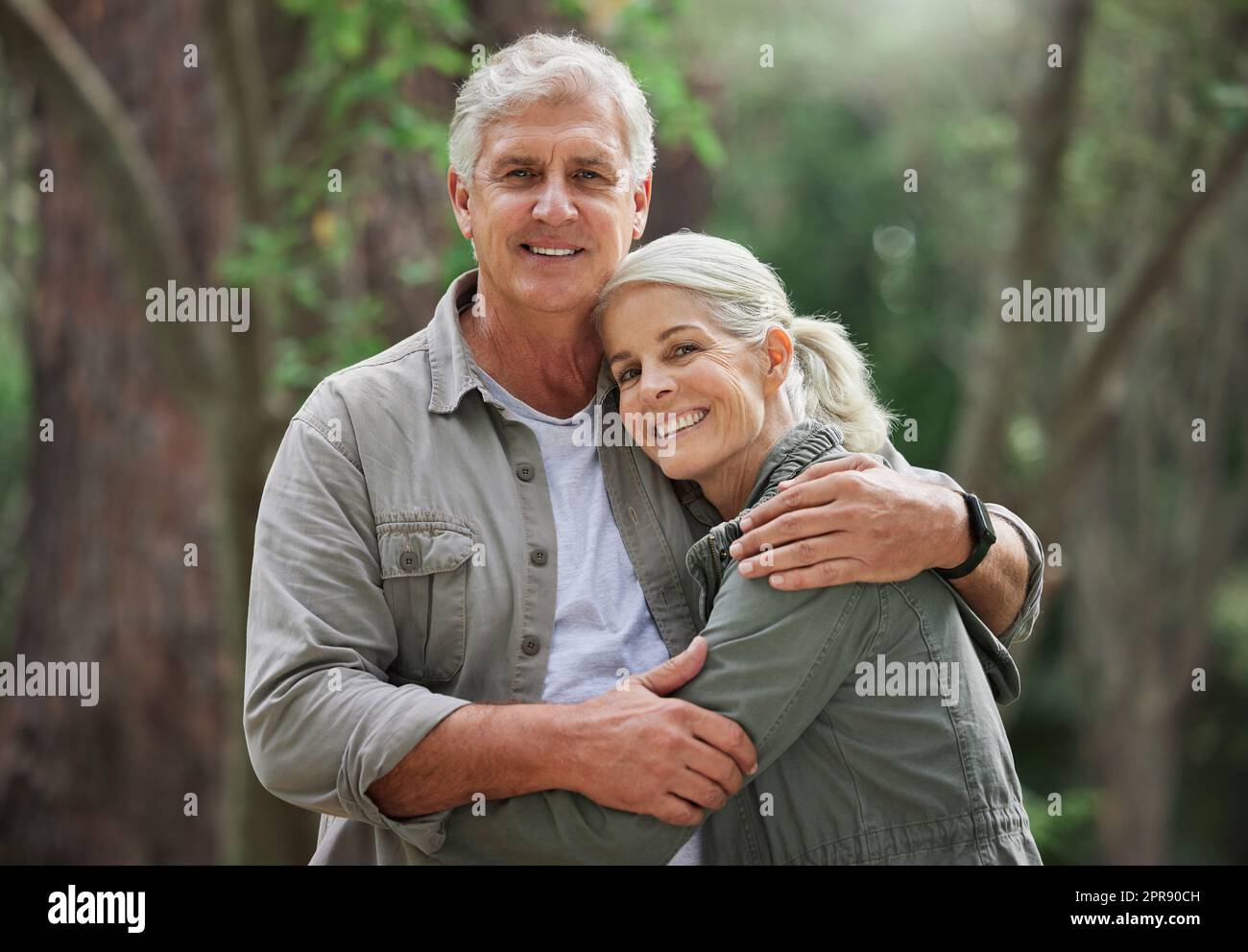 Portrait d'un couple caucasien âgé souriant et regardant heureux dans une forêt pendant une randonnée en plein air. Homme et femme montrant de l'affection et se tenant pendant une pause dans la nature Banque D'Images