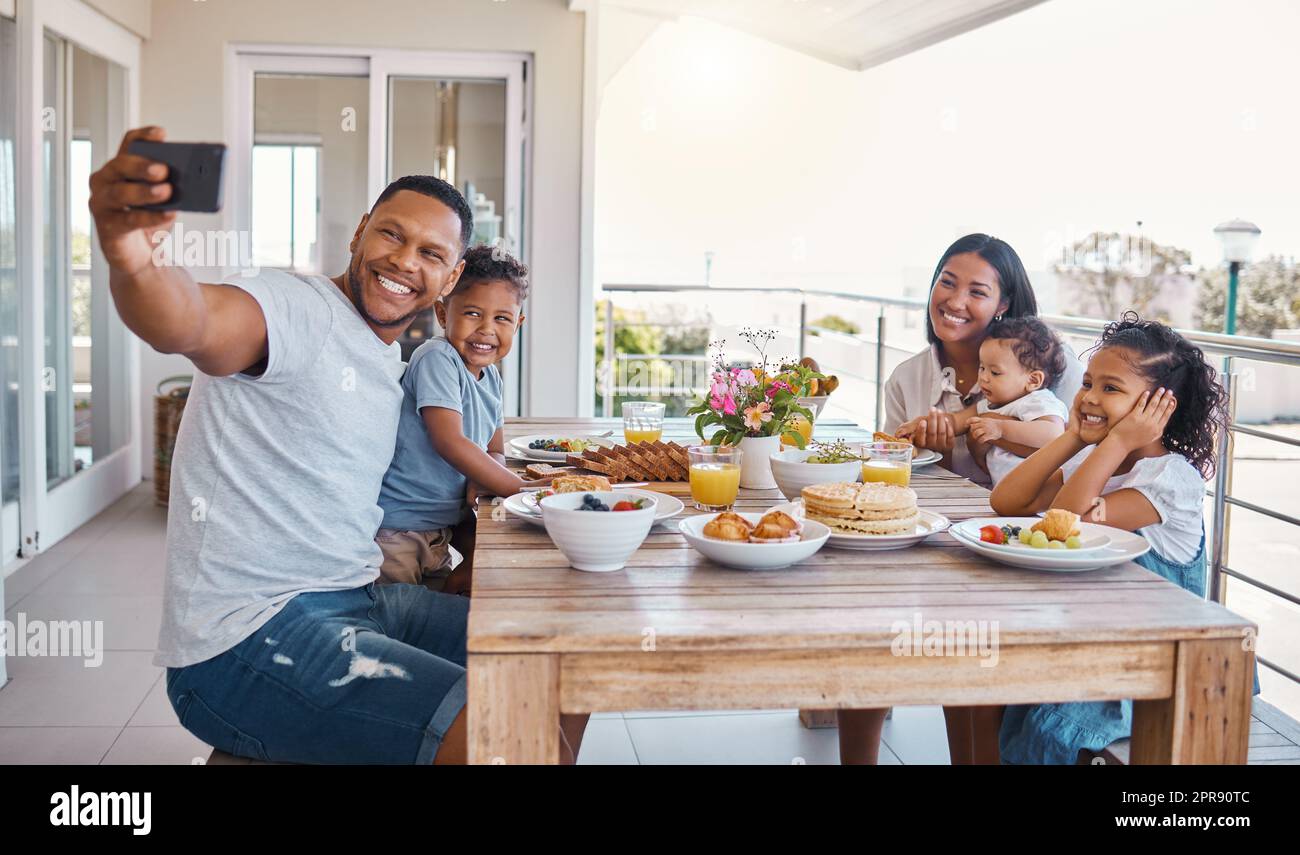 La famille et la nourriture sont tellement amusantes. Une jeune famille prend un selfie tout en déjeunant à la maison. Banque D'Images