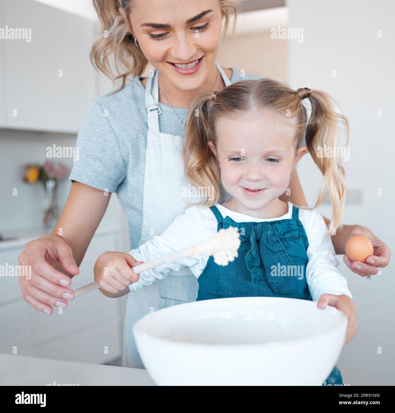 Mère et fille qui cuisent à la maison. Bonne liaison et bonne cuisson de la mère et de l'enfant. Femme aidant sa fille à faire de la pâte. Jeune mère tenant un œuf, faisant cuire avec sa petite fille. Banque D'Images