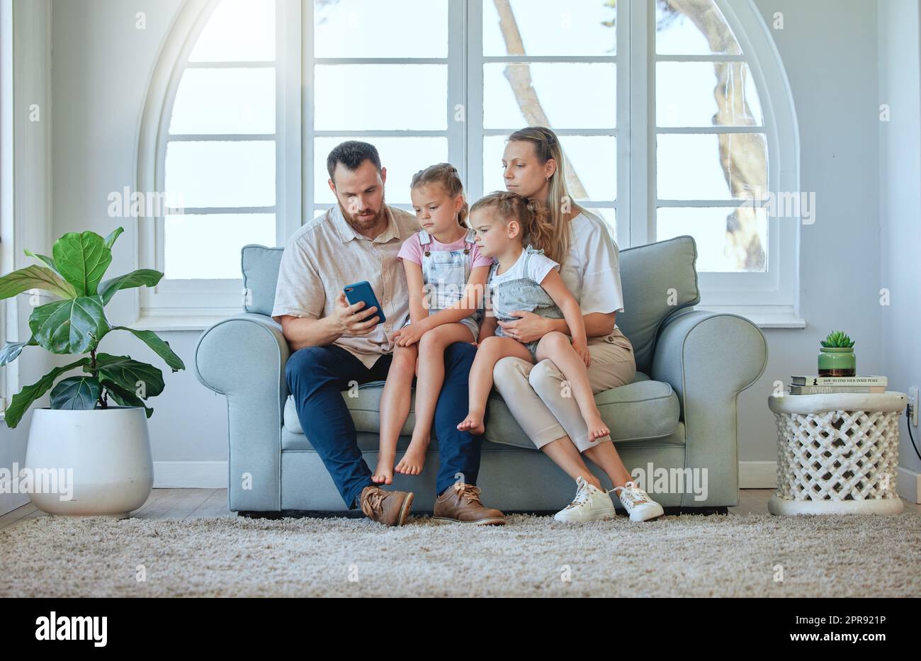 Nous vivons une vie simple. Une jeune famille utilisant un téléphone ensemble à la maison. Banque D'Images