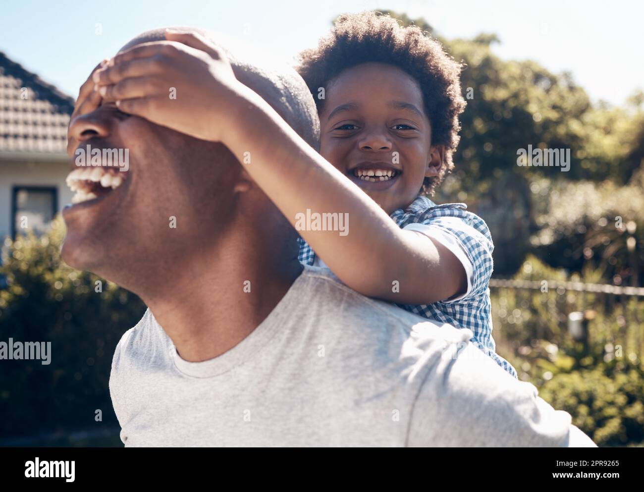 Portrait d'un homme afro-américain heureux en liaison avec son jeune petit garçon à l'extérieur. Deux hommes noirs, père et fils, ont l'air heureux et positifs tout en étant affectueux et en jouant dans une cour Banque D'Images
