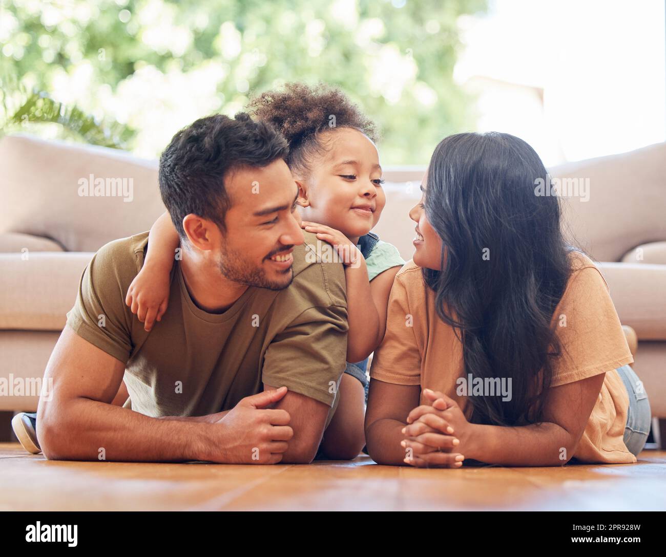 Tellement d'amour dans une seule photo. Photo en longueur d'une jeune famille affectueuse de trois personnes qui se trouve à l'étage du salon à la maison. Banque D'Images