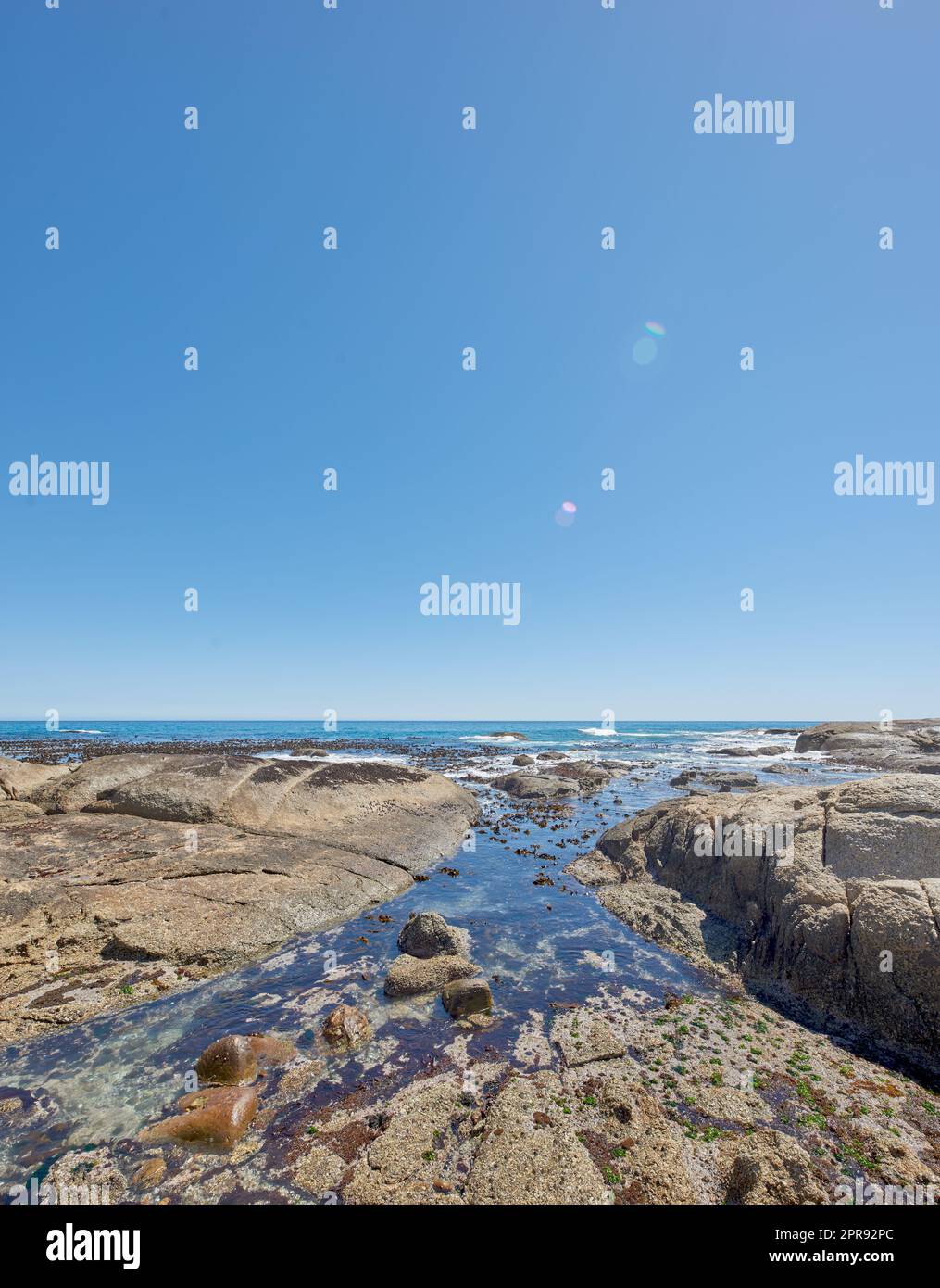 Copiez l'espace en mer avec un fond ciel bleu clair et une côte rocheuse à camps Bay, le Cap, Afrique du Sud. Rochers sur une plage au bord d'un océan majestueux. Paysage pittoresque pour des vacances d'été Banque D'Images
