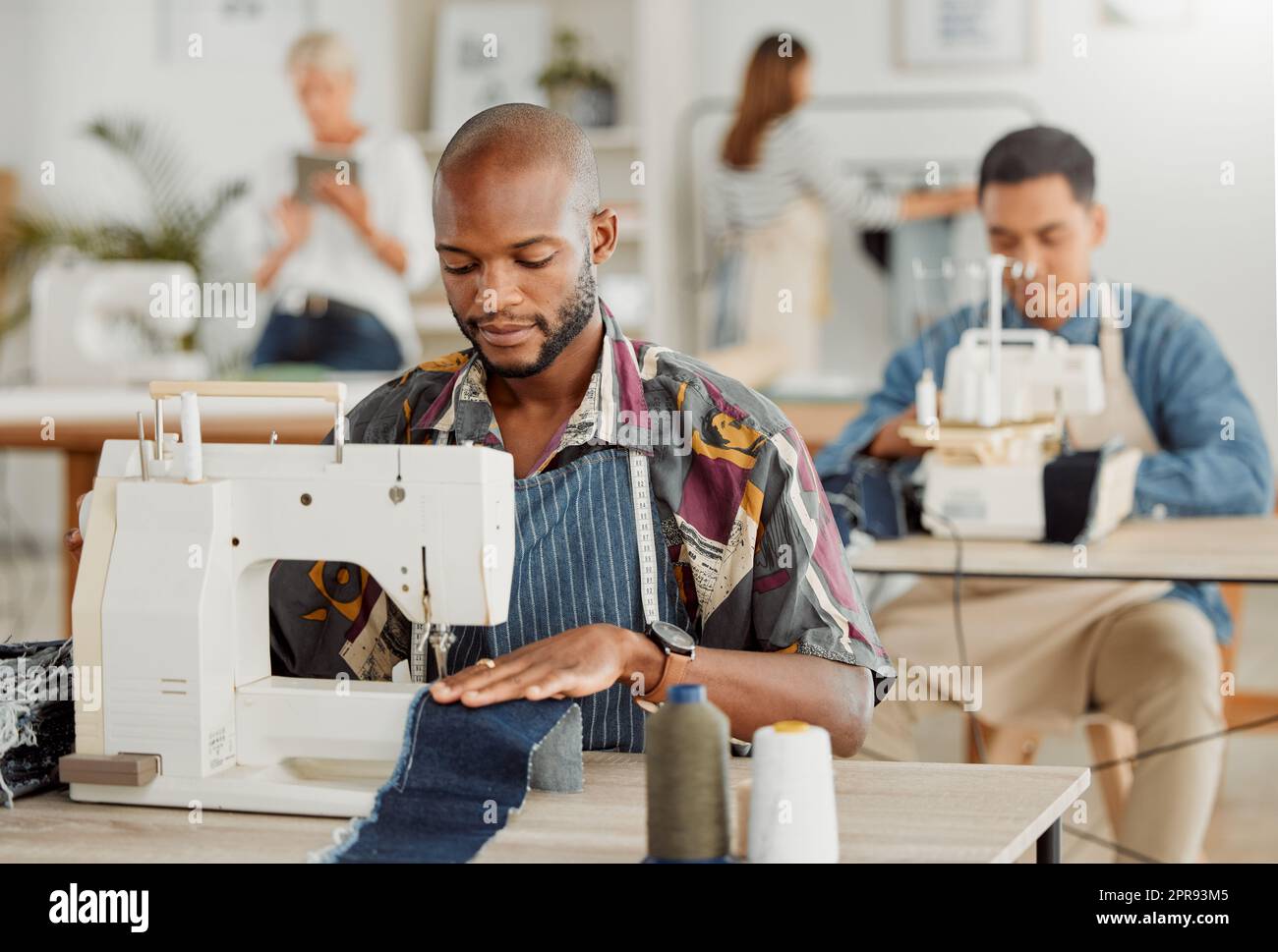 Mode, design et styliste ou un jeune designer travaillant avec machine à coudre. Employé d'affaires occupé et créatif créant de nouveaux vêtements, tendance et tendance. Homme au travail avec du matériel dans un atelier. Banque D'Images