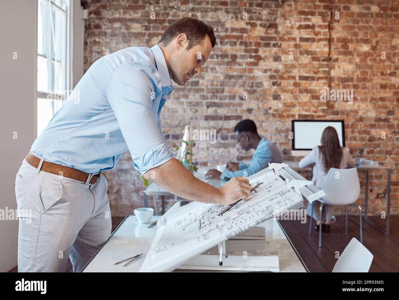 Architecte, ingénieur concepteur ou entrepreneur en bâtiment qui dessine un plan sur une table de dessin pour un projet ou un développement dans son bureau. Un concepteur masculin qui réalise une esquisse de plan dans une entreprise d'architecture Banque D'Images