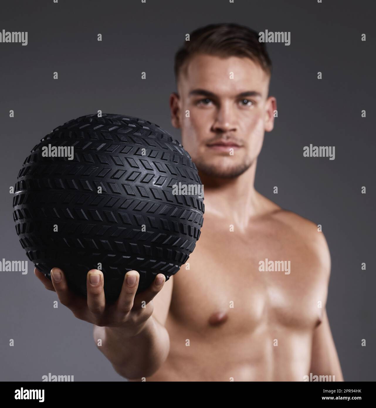 Passons au niveau supérieur de votre entraînement. Un jeune sportif tenant une balle d'exercice tout en se tenant debout sur un fond gris. Banque D'Images