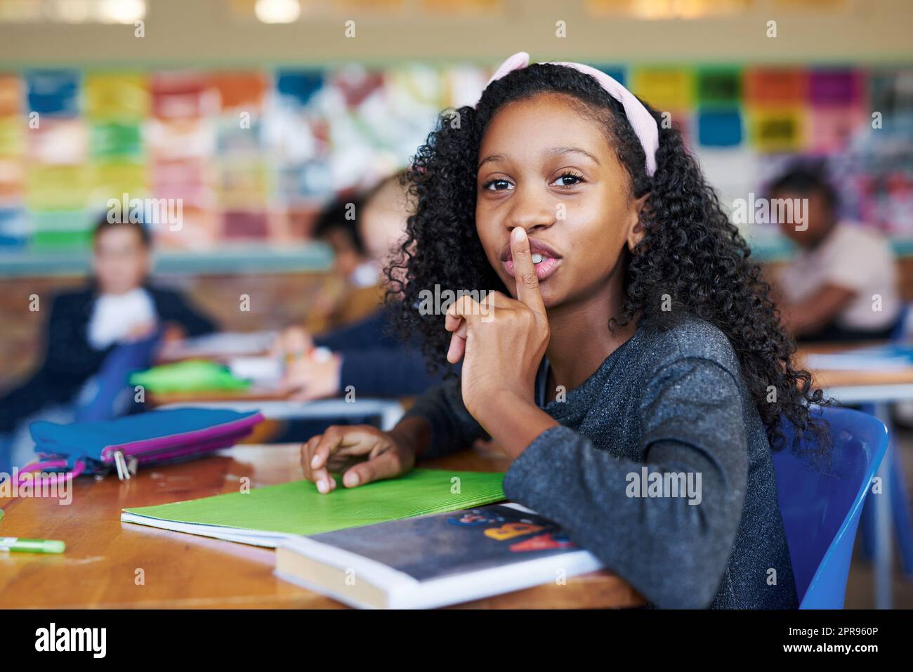 SHH, vous n'êtes pas censé parler. Une jeune fille assise dans sa salle de classe avec son doigt sur ses lèvres dans un geste de précipitation. Banque D'Images