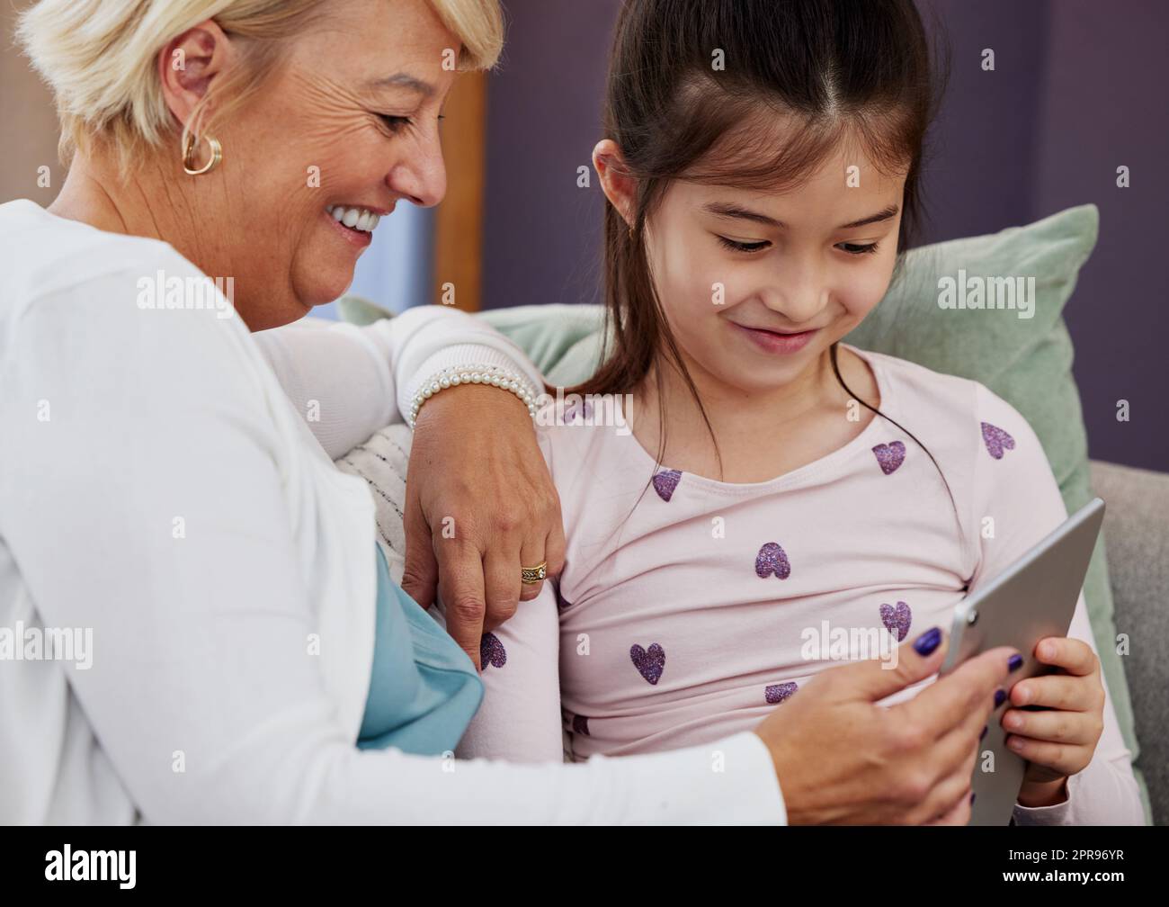 Testons maintenant votre intelligence, gran. Une adorable petite fille utilisant une tablette numérique tout en étant assise à la maison avec sa grand-mère. Banque D'Images