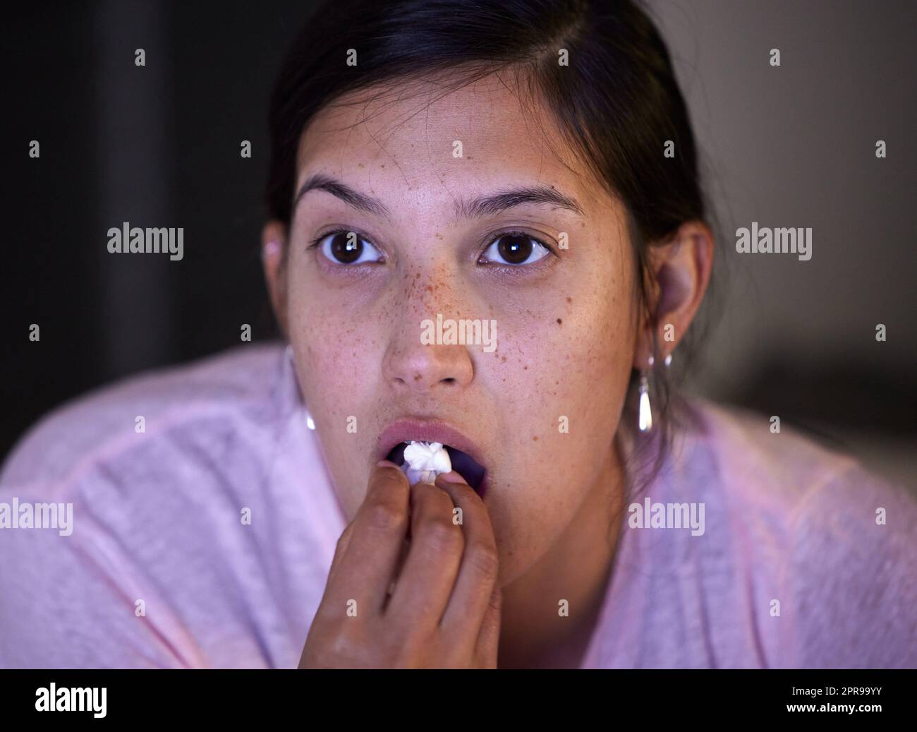 L'intrigue s'épaissit. Une jeune femme mangeant du pop-corn tout en regardant la télévision à la maison. Banque D'Images