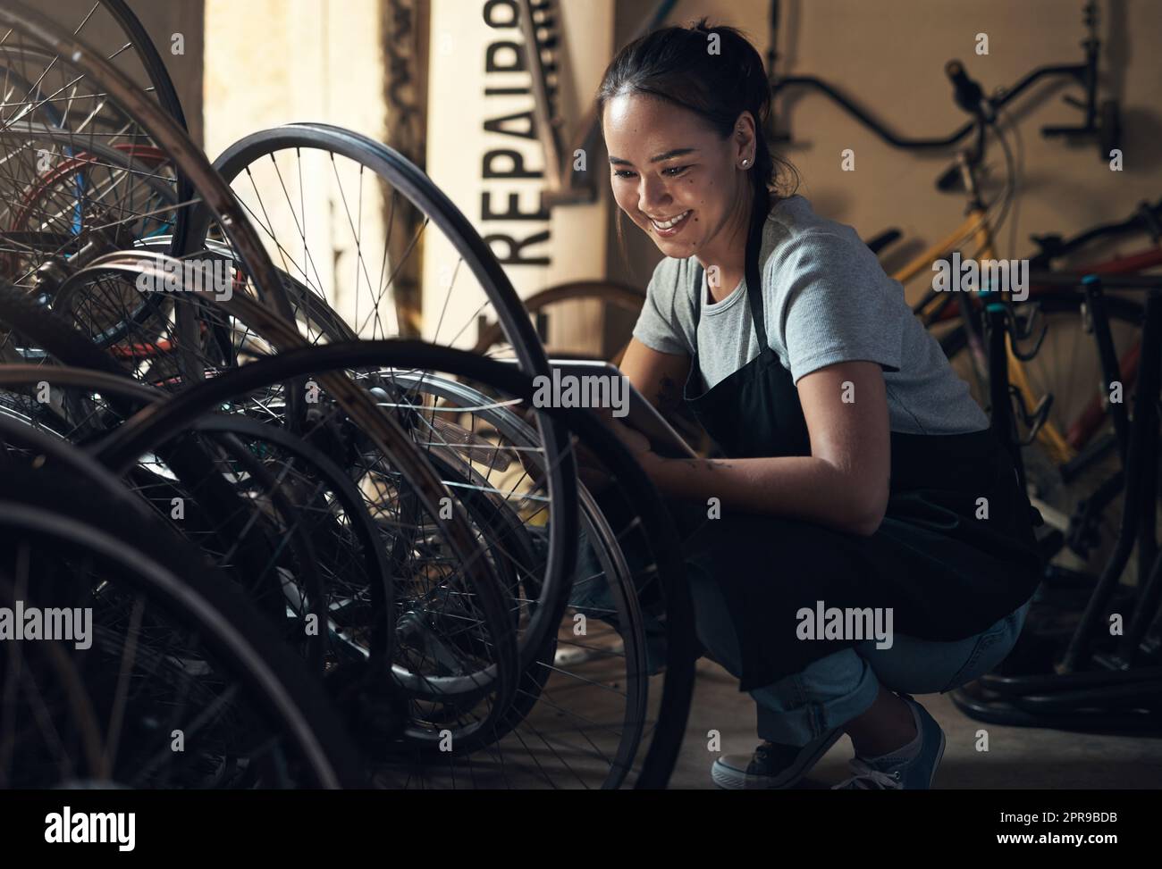 Le maquillage ne m'a jamais ravie. Une jeune femme heureuse qui fixe un vélo dans un atelier de réparation de vélos. Banque D'Images