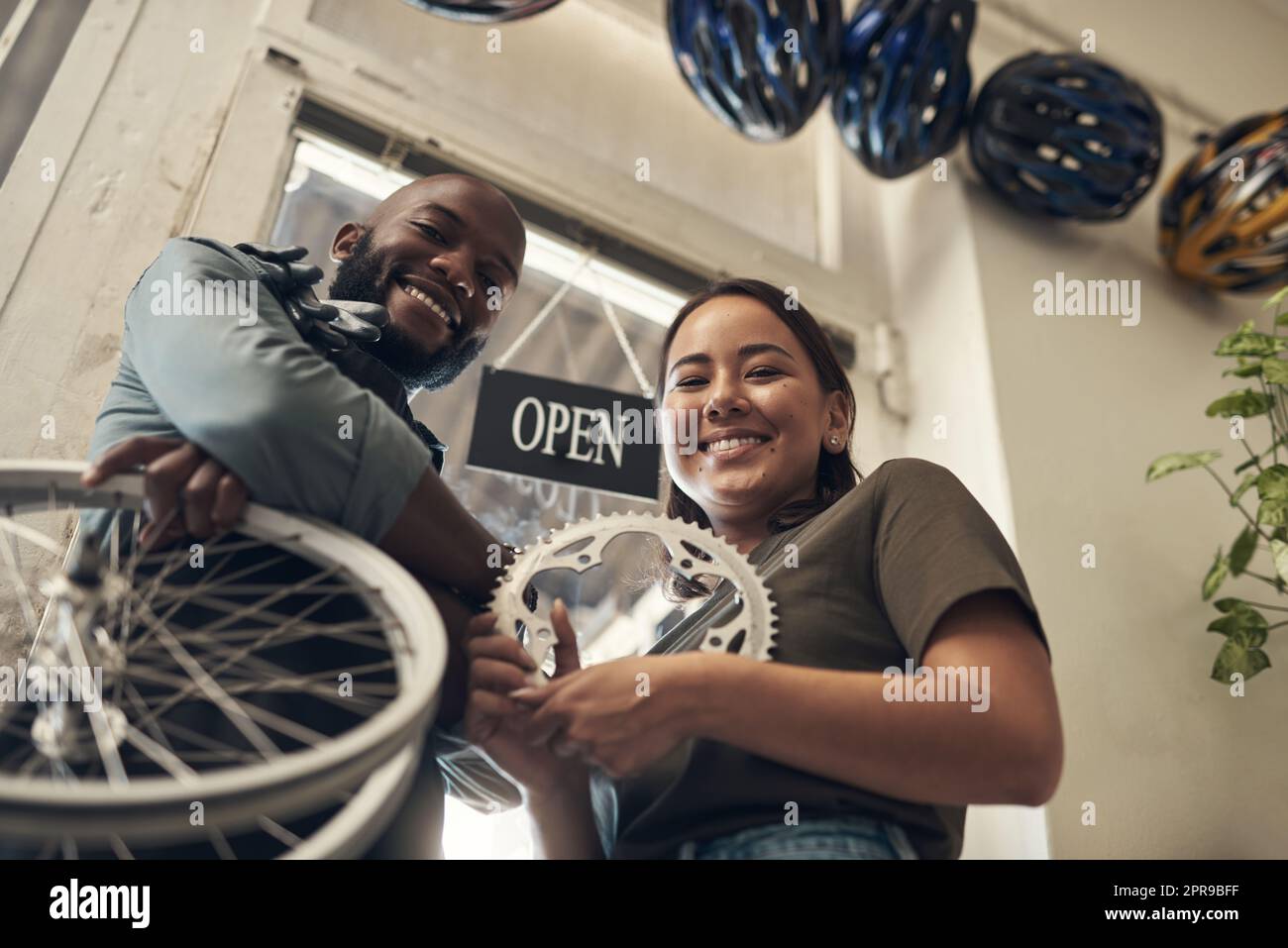 Laissez-nous nous réparer. Photo à angle bas de deux jeunes propriétaires d'entreprise se tenant ensemble dans leur magasin de vélos et tenant des pièces de rechange. Banque D'Images