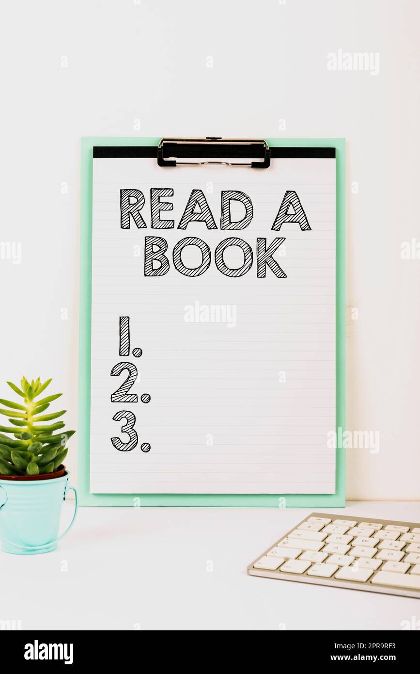 Inspiration montrant le signe Lire Un livre. Vitrine d'affaires Profitez de la littérature activité traditionnelle Apprenez de nouvelles choses important message présenté sur le presse-papiers sur le bureau avec fleur et clavier. Banque D'Images