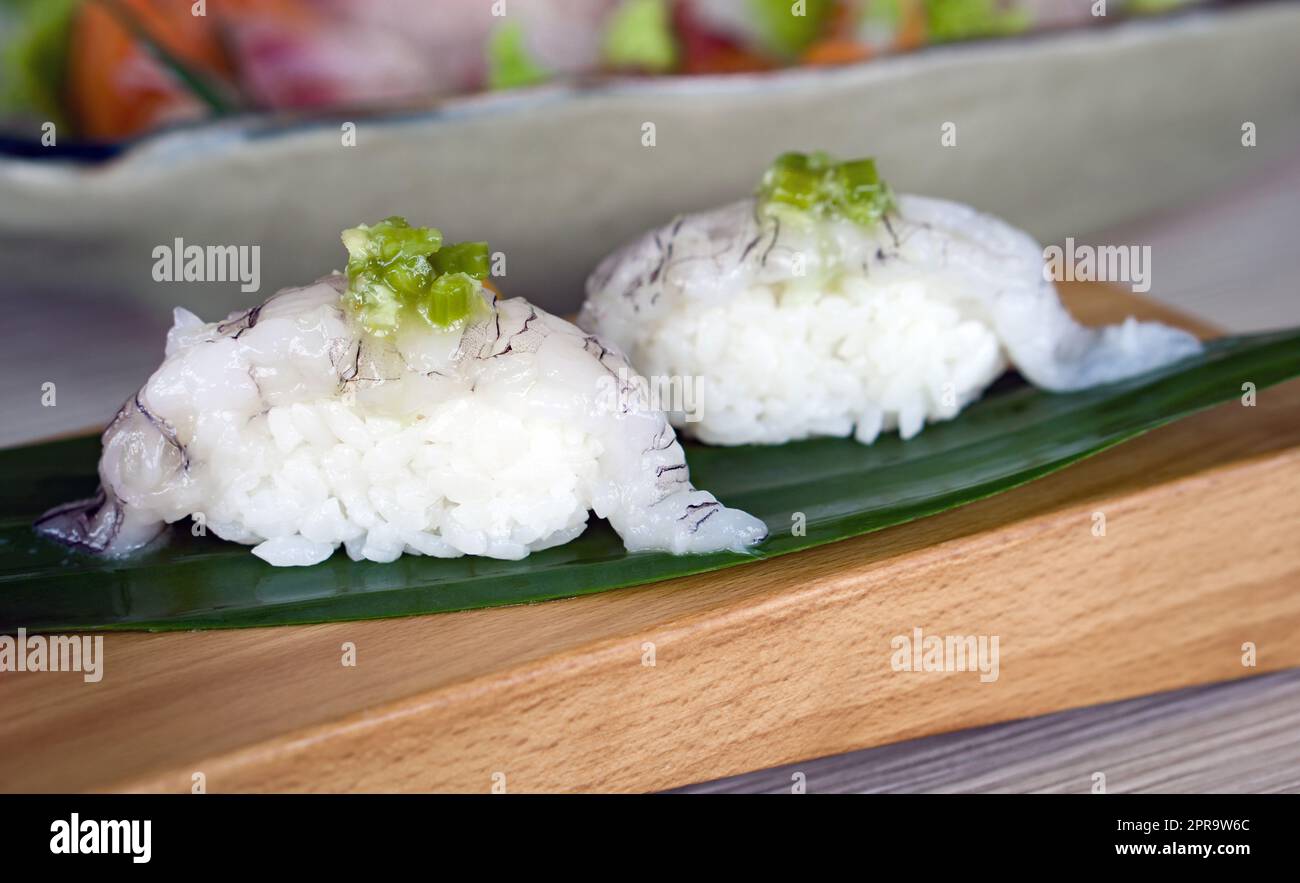 Garniture de sushis shako au wasabi mariné servi sur une assiette en bois décorée de feuilles de bambou. Banque D'Images