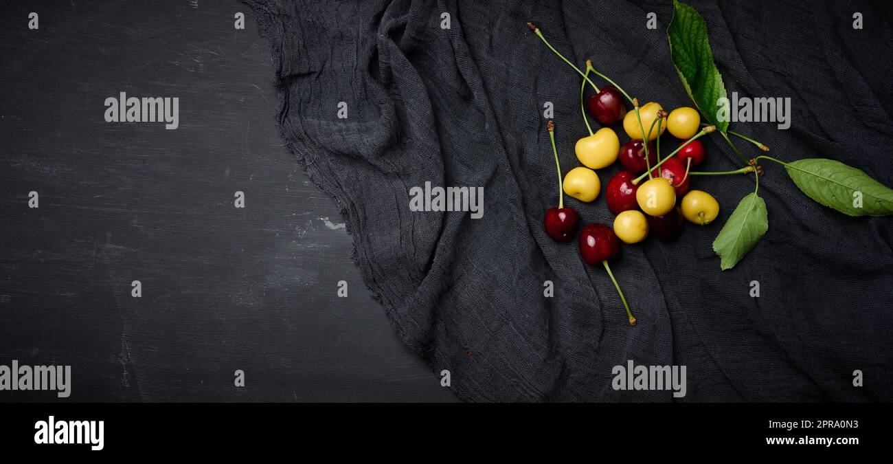 Cerises mûres rouges et jaunes sur fond noir. Baies d'été Banque D'Images