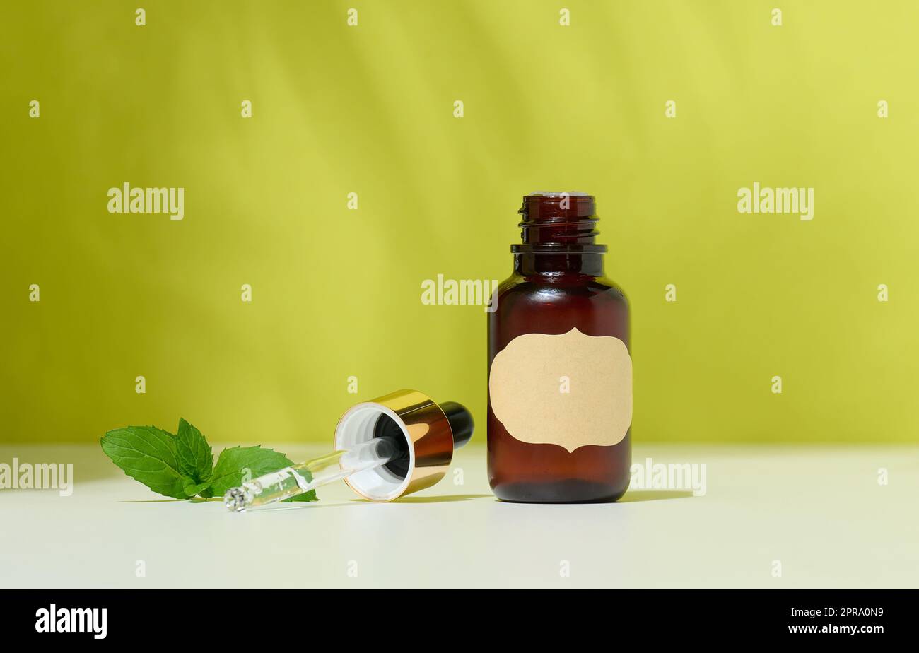 Bouteille en verre brun avec un produit cosmétique et une pipette avec une goutte, fond vert. Récipient pour huiles, gels, acides Banque D'Images