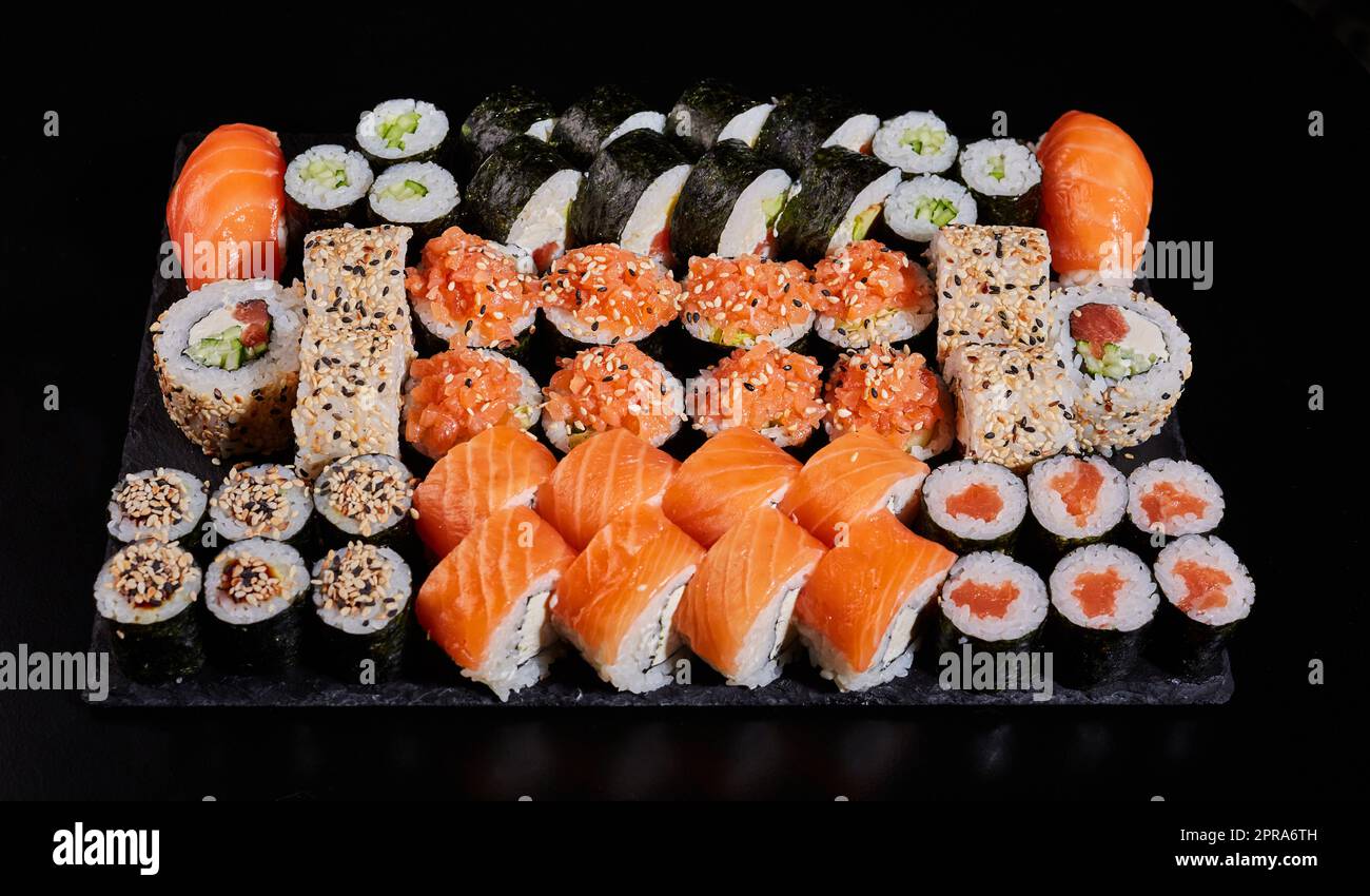 Assortiment de différents types de rouleaux de sushis placés sur un panneau en pierre noire. Banque D'Images