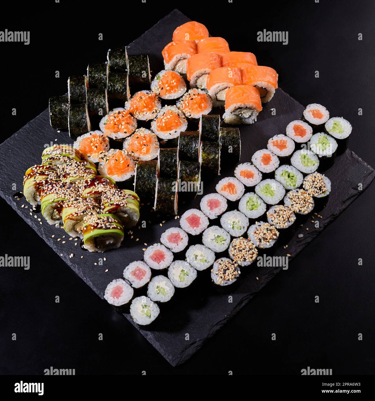 Assortiment de différents types de rouleaux de sushis placés sur un panneau en pierre noire. Banque D'Images