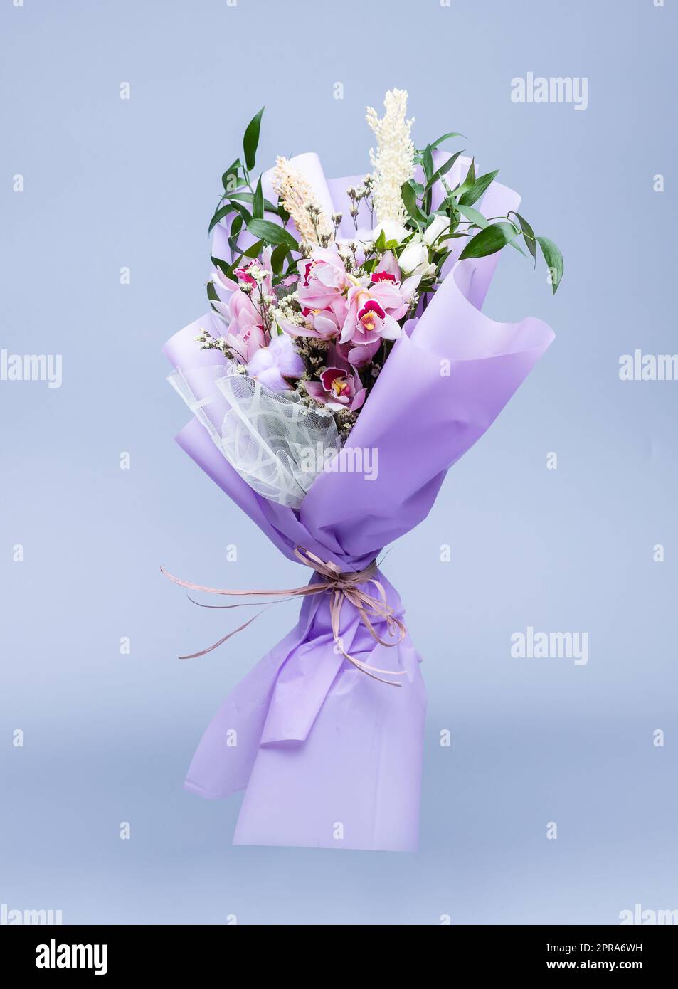 Bouquet de fleurs naturelles enveloppées de papier à tracer floral dans un vase sur fond bleu. Banque D'Images