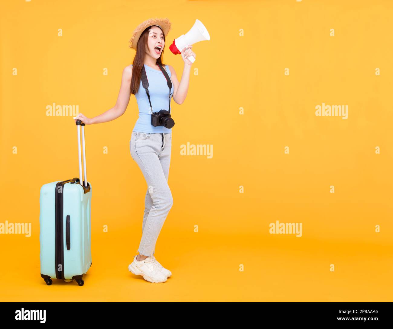 Bonne jeune femme avec des bagages et tenant le mégaphone isolé sur fond jaune, été, concept de voyage. Banque D'Images